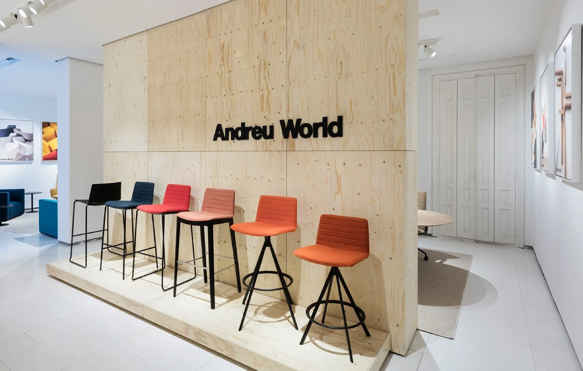 Andreu World showroom featuring a long wooden conference table paired with elegant black ergonomic chairs in a bright, modern office setting.